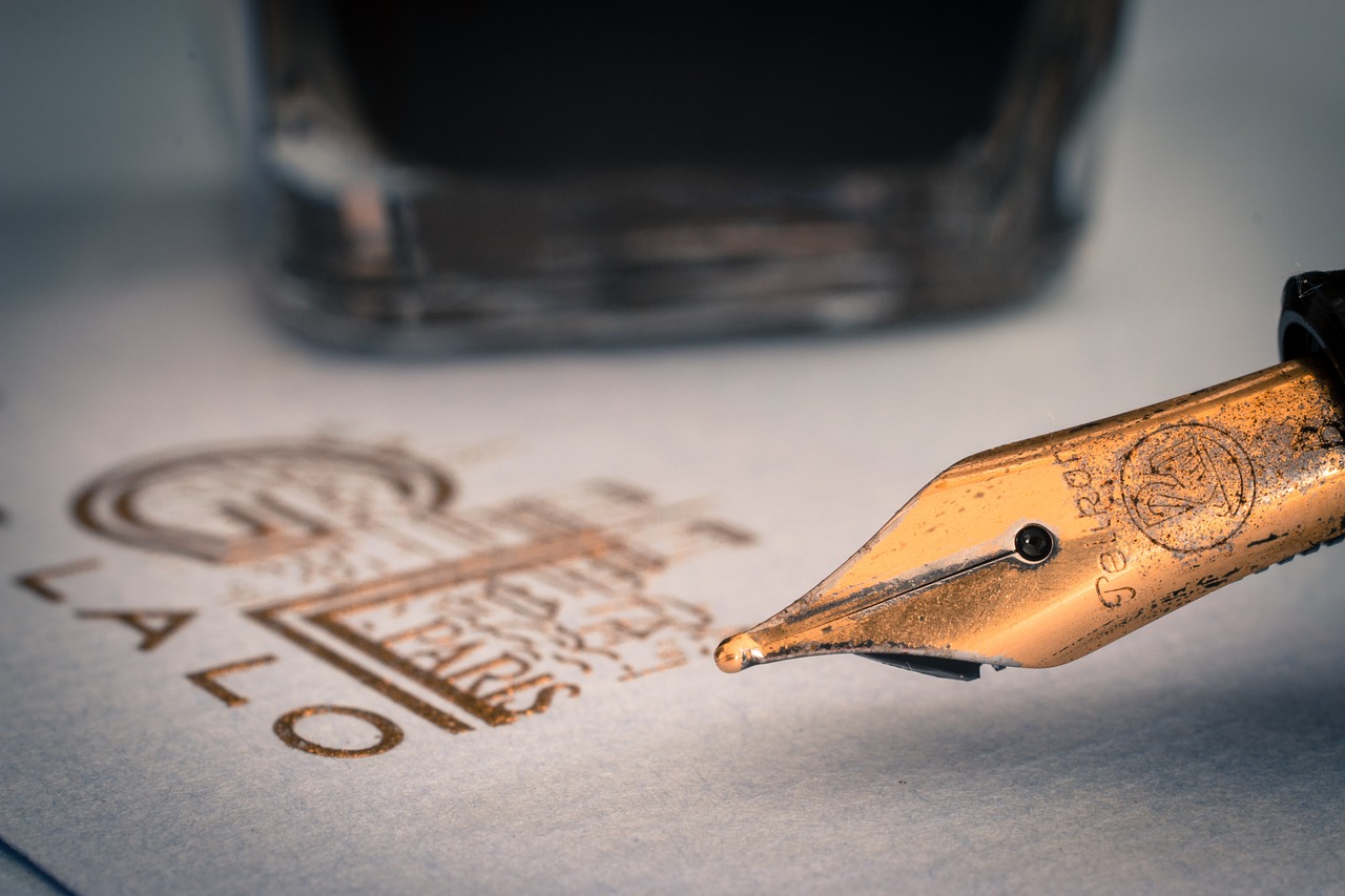 Brass fountain pen nib next to logo and inkwell
